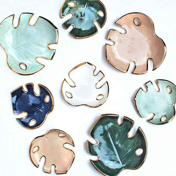 A collection of ceramic leaf bowls, in the shape of a Monstera leaf. In aqua, white, pink and green glazes with gold edges.