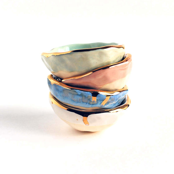 Four stacked ring bowls with gold edges. In aqua, pink, blue and white colors. 