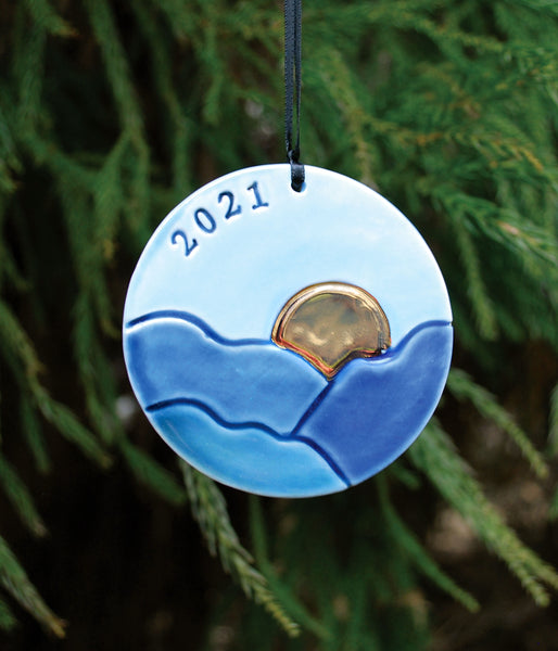 round ornament with blue ridge mountains and golden sun, with year stamped in black. 
