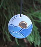 round ornament with blue ridge mountains and golden sun, with year stamped in black. 