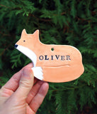 Ceramic ornament, shaped like a fox. Glazed in orange and white. With name stamped in black. 