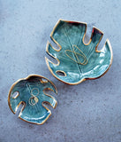 Handmade ceramic monstera-leaf shaped bowl. In dark green glaze, with gold luster around the edges. 