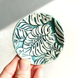 Circle shaped ring dish, with impressed monstera-leaf pattern. In white and green glazes. 