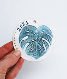 Monstera Leaf Ornament, 2023Monstera leaf ornament, in green and white. 2023 is stamped. Add metallic gold luster for a special shine on your tree. This ornament can also be customized with a n